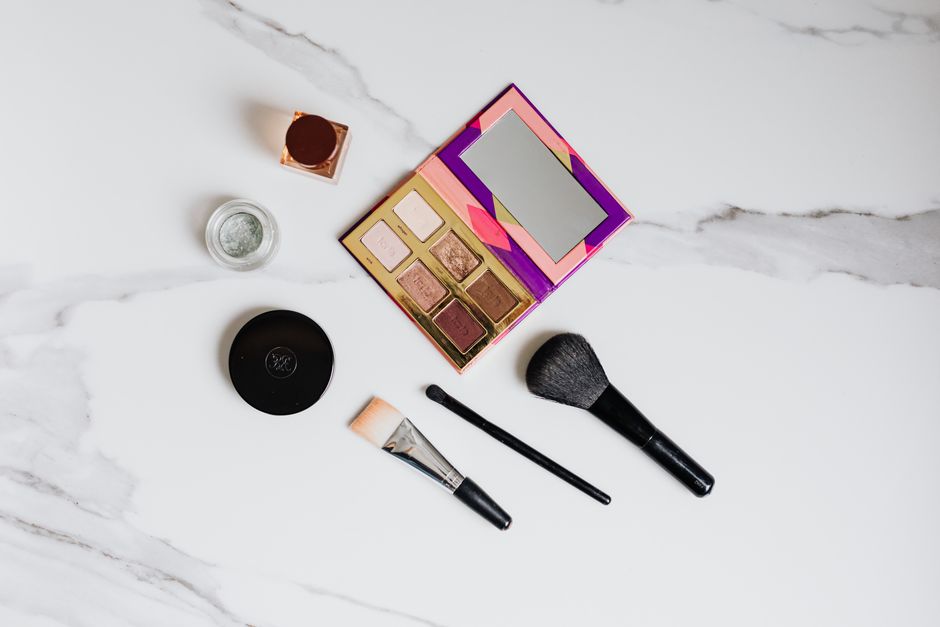 Flat lay of makeup essentials on a marble background, showcasing brushes and eyeshadow palette.
